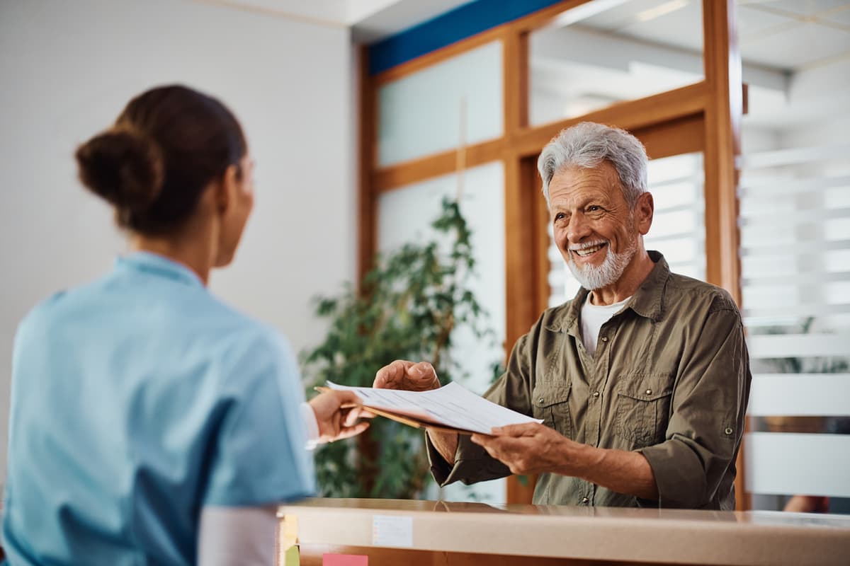 A smiling patient checking in with a receptionist at the front desk